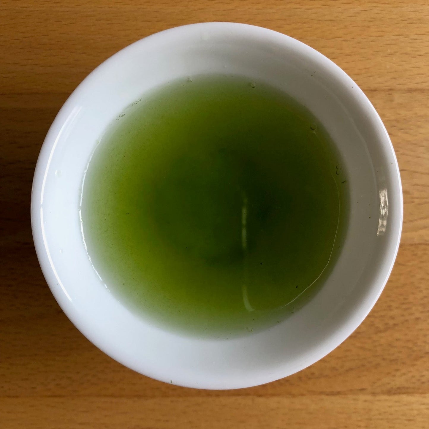 Saemidori 2026 sencha brewed in a larger white bowl, top-down view — vivid bright green liquor