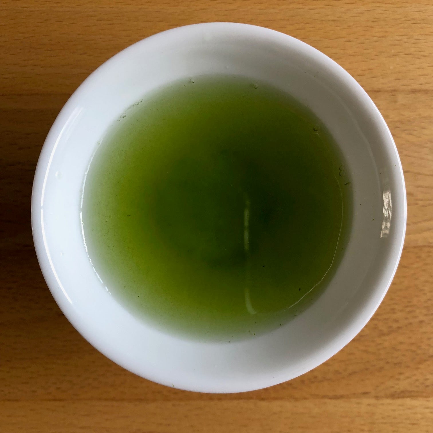Saemidori 2026 sencha brewed in a larger white bowl, top-down view — vivid bright green liquor