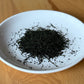Dried Hoshino Shizuku 2026 sencha leaves on a white plate, top-down view — fine dark-green needle-shaped leaves