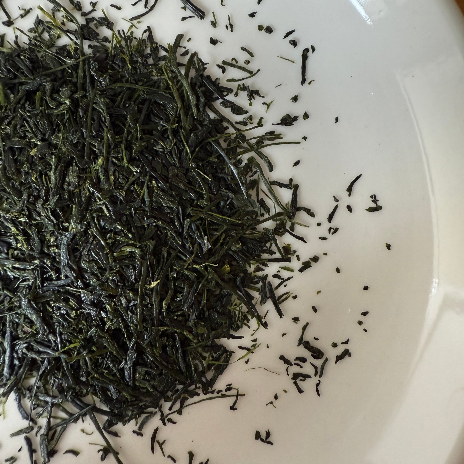 Close-up of dried Hoshino Shizuku 2026 sencha leaves on a white plate, showing the fine needle-like leaf shape