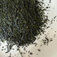 Close-up of dried Hoshino Shizuku 2026 sencha leaves on a white plate, off-centre composition